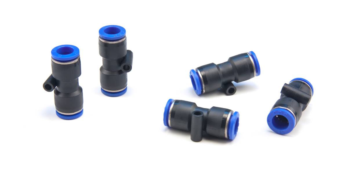 Five push-to-connect fittings lay on a white background. They are black with a blue ring on either end to connect pipes and tubes.