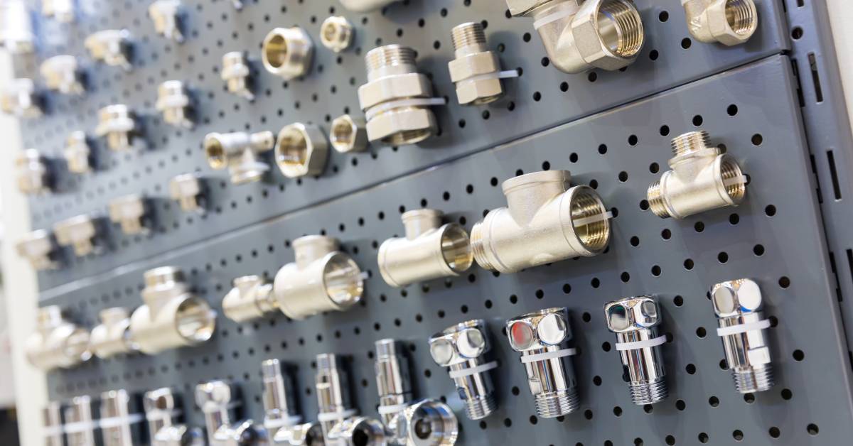 Many different brass and steel pipe fittings for hydraulic and pneumatic systems fastened to a pegboard.