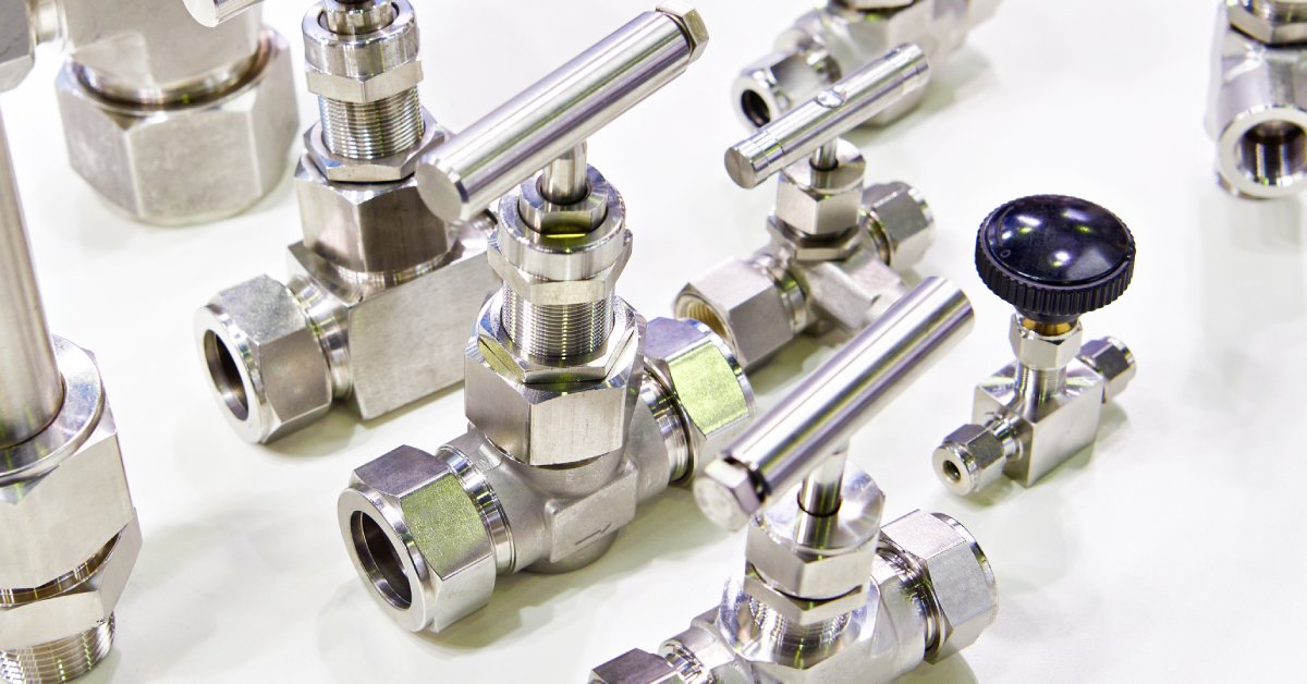 A white table with several types of ball valves in different sizes. All of them are stainless steel.