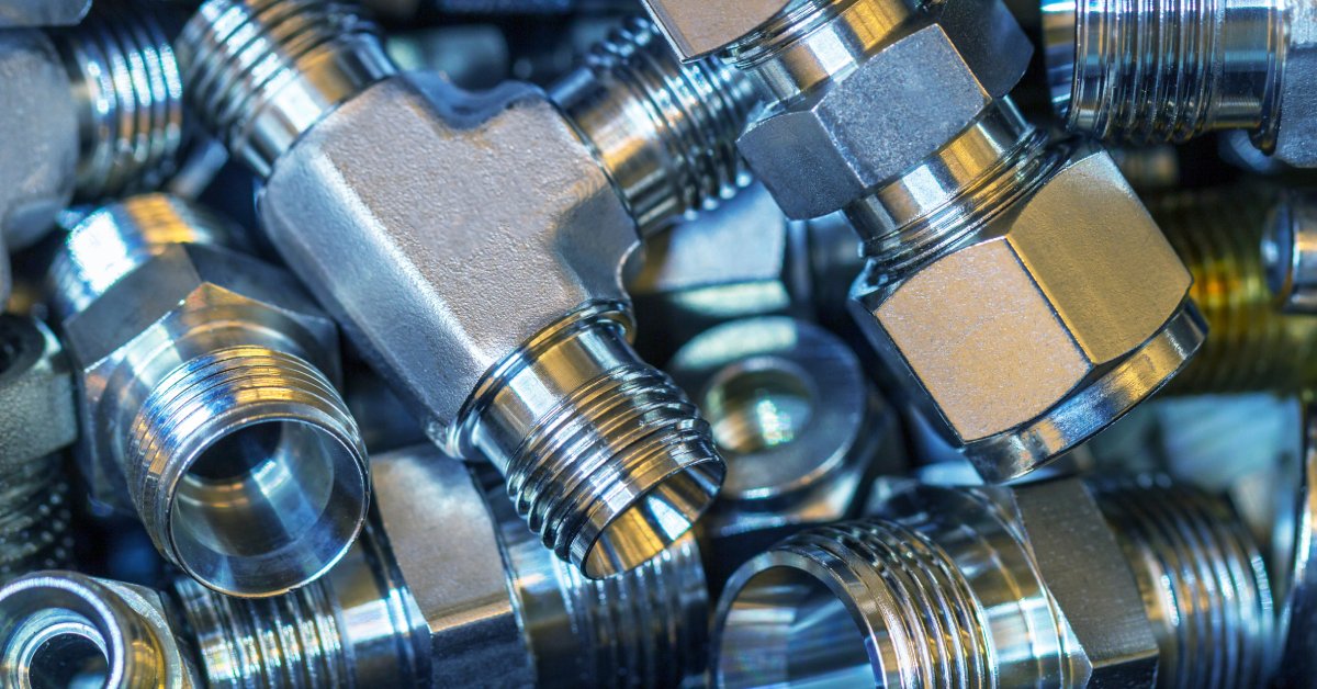 A close-up of a pile of hydraulic hose fittings. The fittings are all made from steel and come in different shapes and sizes.