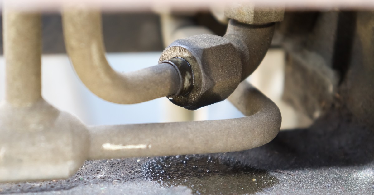 A pipe to a system's equipment is leaking. You can see a fluid making a small puddle under the bolt where it is connected.