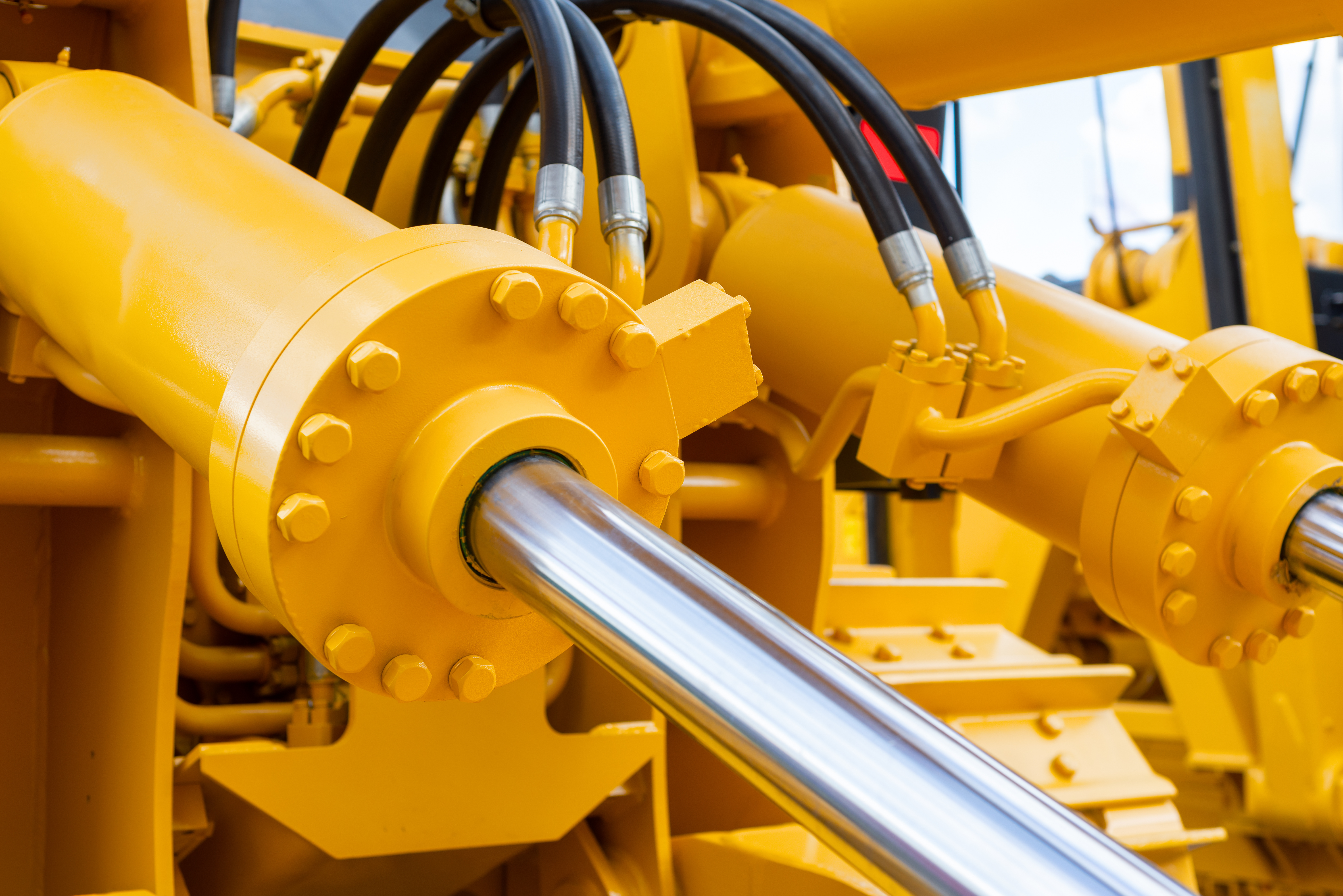 Big yellow hydraulic cylinders are powering construction equipment. The cylinders are connected with black wires at the top.