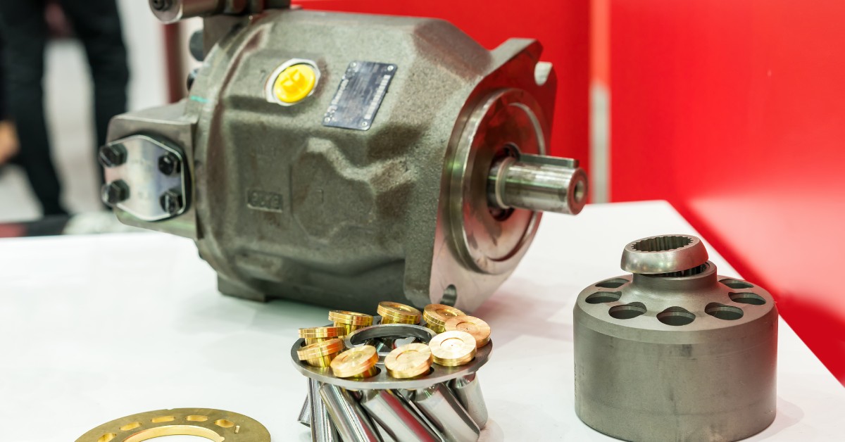 A piston hydraulic pump is on a white table. The inside components of the pump are on display in front of the whole part.