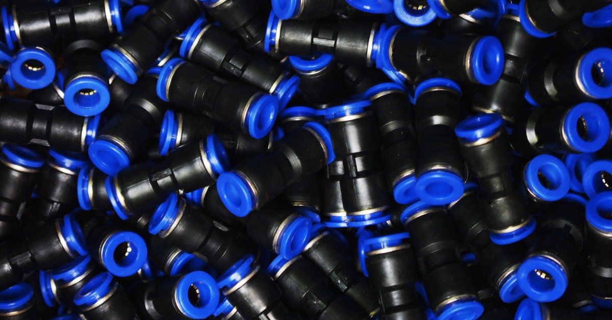 A close-up of a pile of push-to-connect pipe fittings. The components are black with a blue connector on the inside.