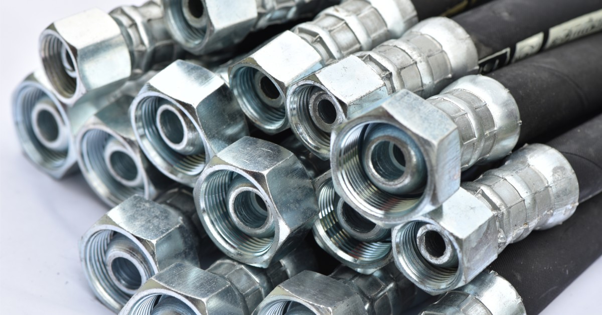 A pile of hydraulic hoses on a white table. The hoses are black with stainless steel fittings on the end.