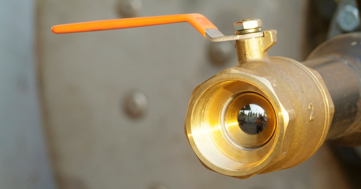 A close-up of a hydraulic ball valve. There is an orange lever and the inside of the valve is visible.