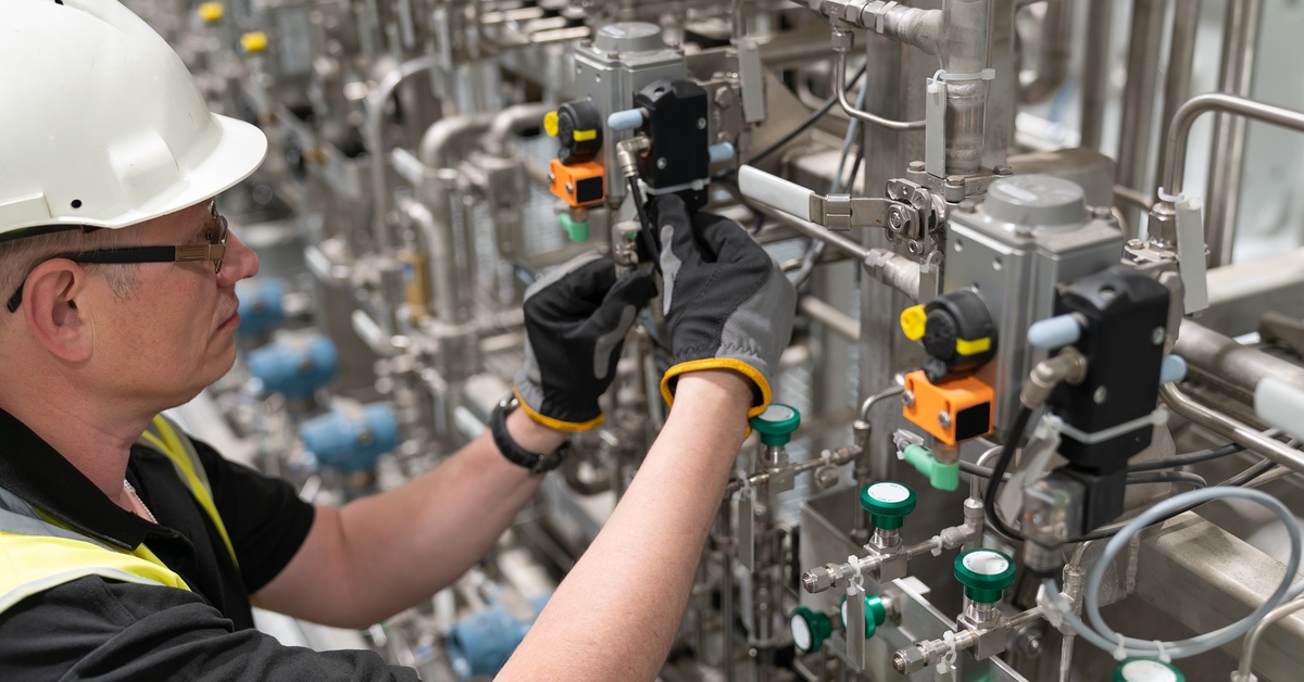 A close-up of a male engineer, wearing safety gear, checking on the pneumatic valves in the manufacturing plant.