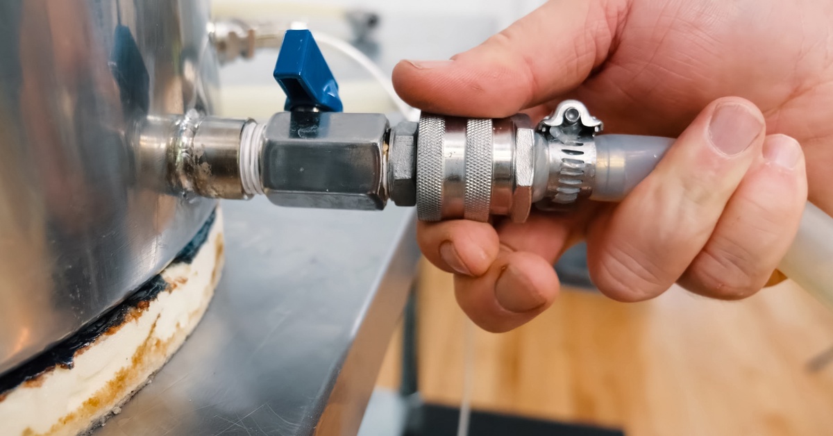 A close-up of a person's right hand as they complete plumbing work using a ball valve and pipe adapters on a tank.