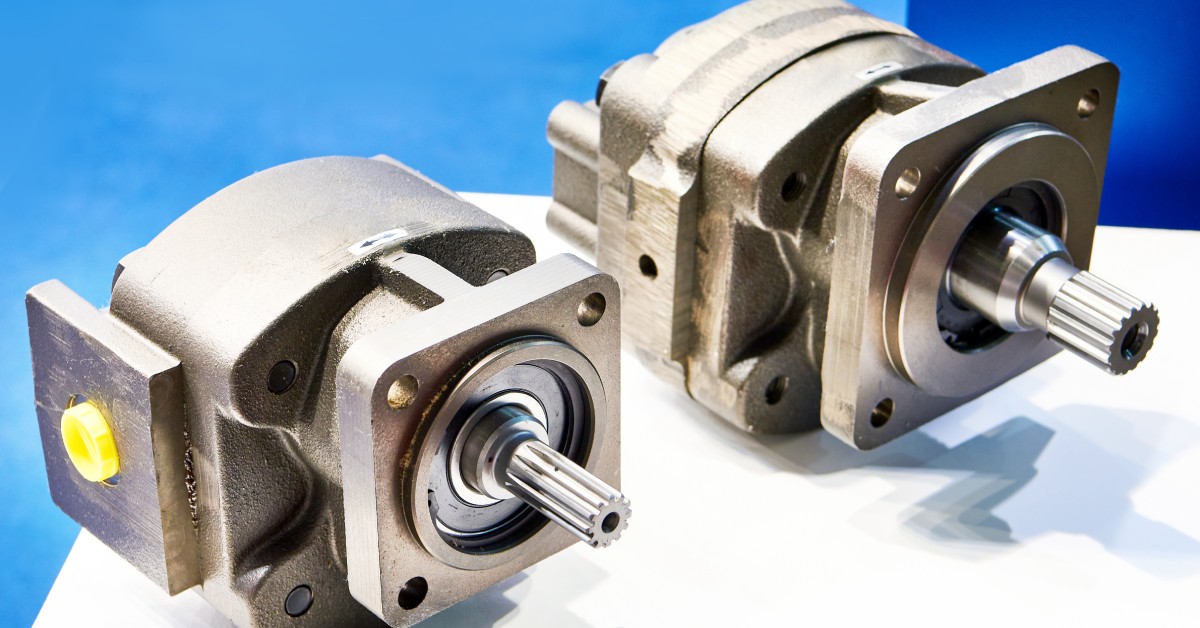 A pair of hydraulic motors and pumps sit side by side on a white surface against a plain blue background.
