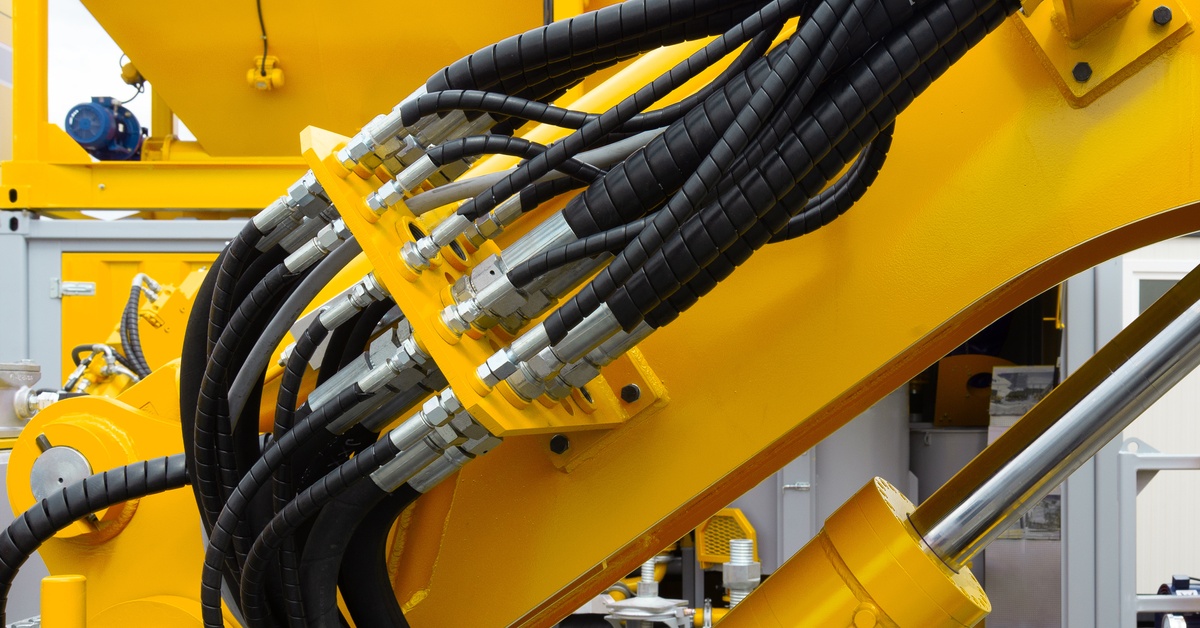 A yellow industrial machine with hydraulic components, including a pump, fittings, hoses, and tubes.
